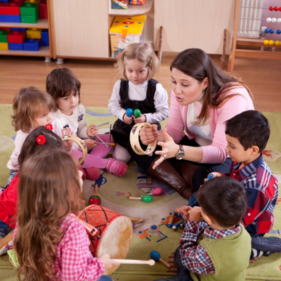 Une animatrice et de jeunes enfants jouant de la musique en cercle dans une classe de maternelle.